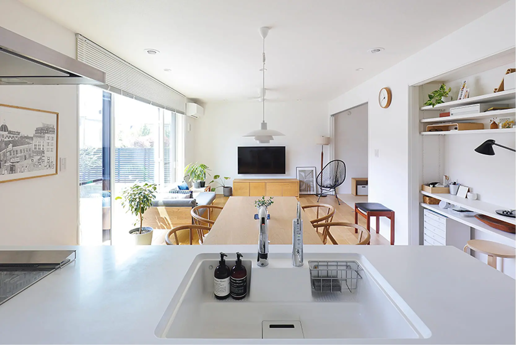 明るい自然光が差し込むリビングダイニングで、木製家具と観葉植物が調和する北欧風の空間