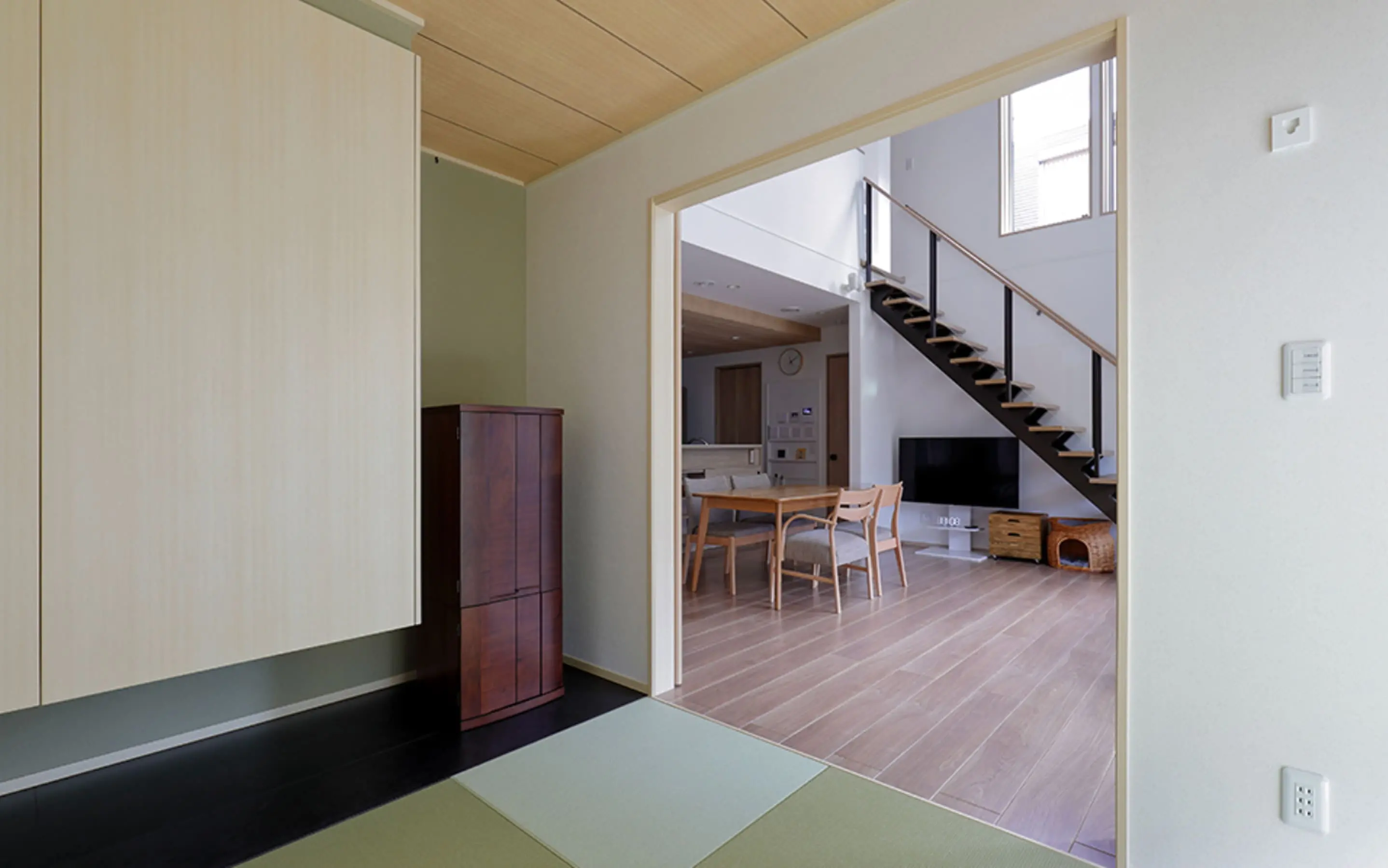 畳の和室からリビングを望む視点で、シンプルな収納と木目の天井が落ち着いた雰囲気を演出