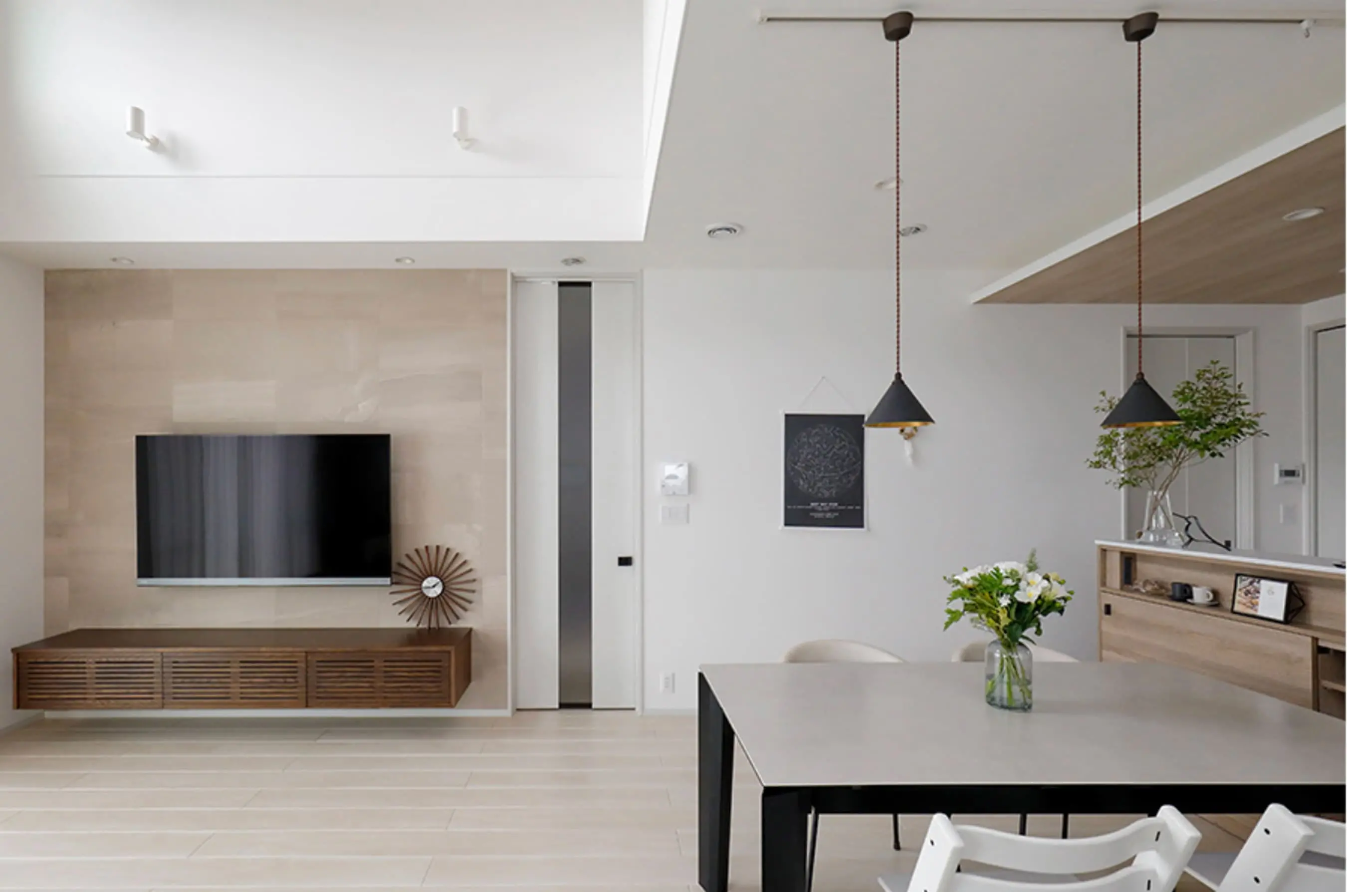 テレビが壁掛けされたリビングの一角で、ペンダントライトや観葉植物がアクセントに