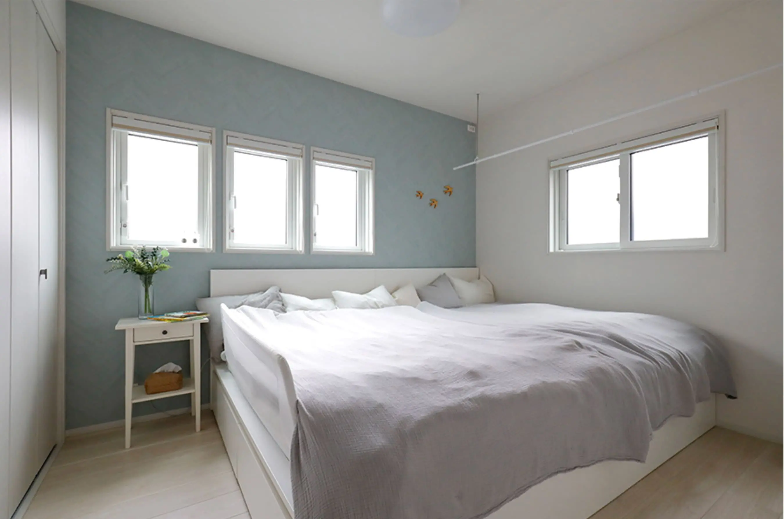 水色のアクセントクロスと4つの窓が並ぶ明るい寝室に、大きなベッドが設置されている