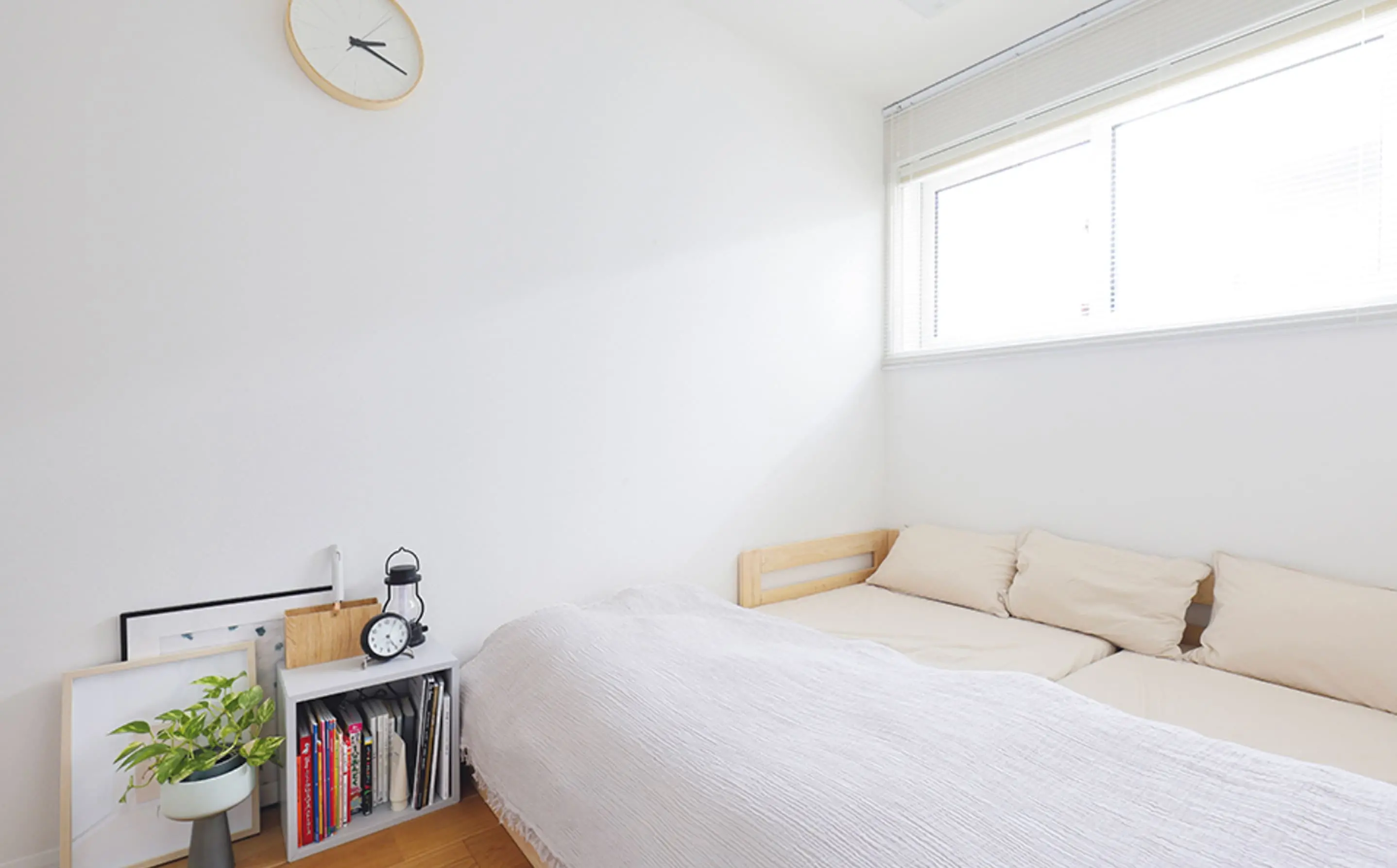 シンプルなベッドと小さな本棚が置かれた寝室で、白を基調にした落ち着いた空間