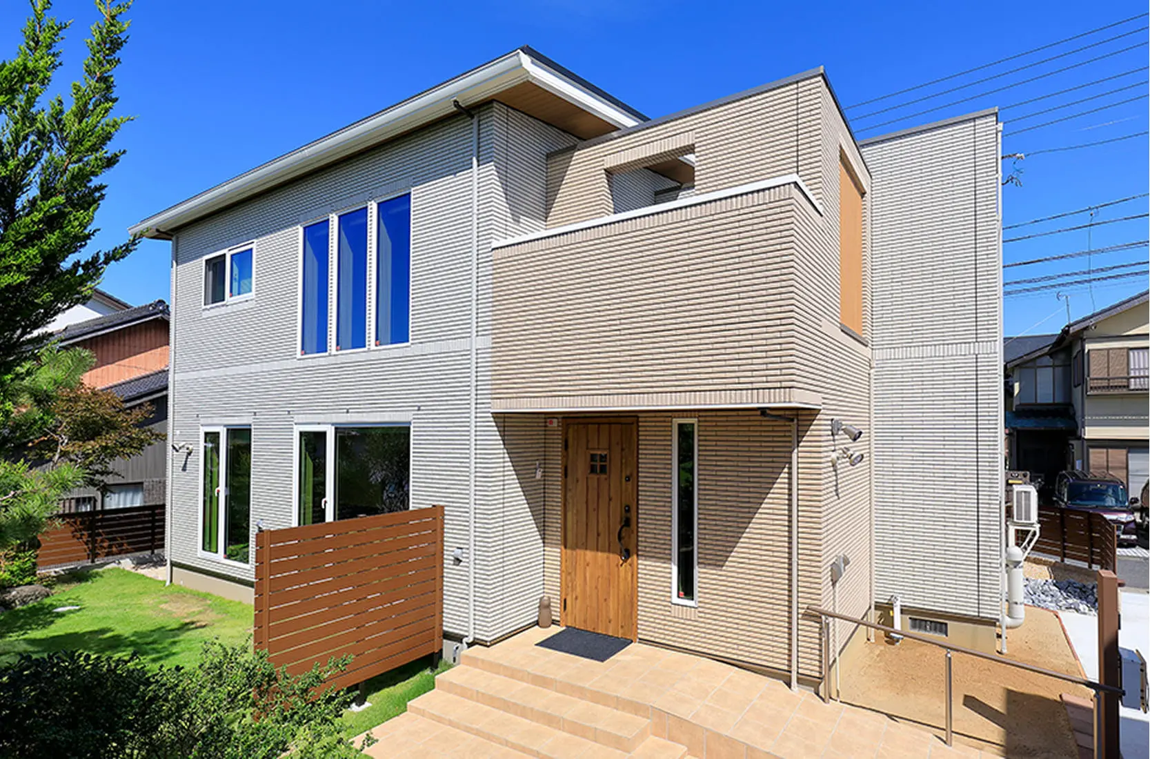 ベージュ系タイル外壁と木製ドアが特徴の、庭付き2階建て一戸建て住宅の外観