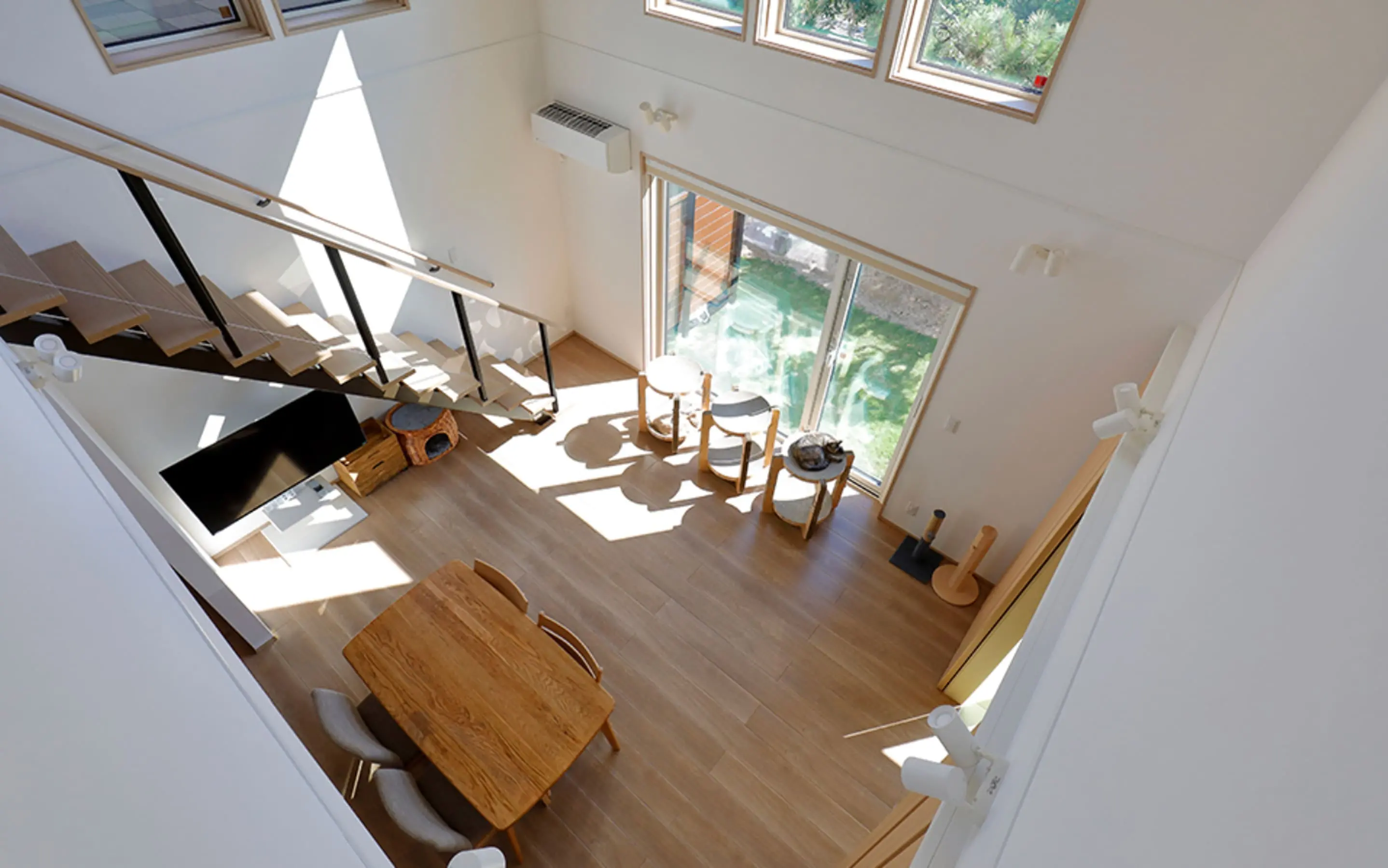 上階から見下ろしたリビングの全景で、キャットタワーやテレビ、ダイニングテーブルが並ぶ明るい空間