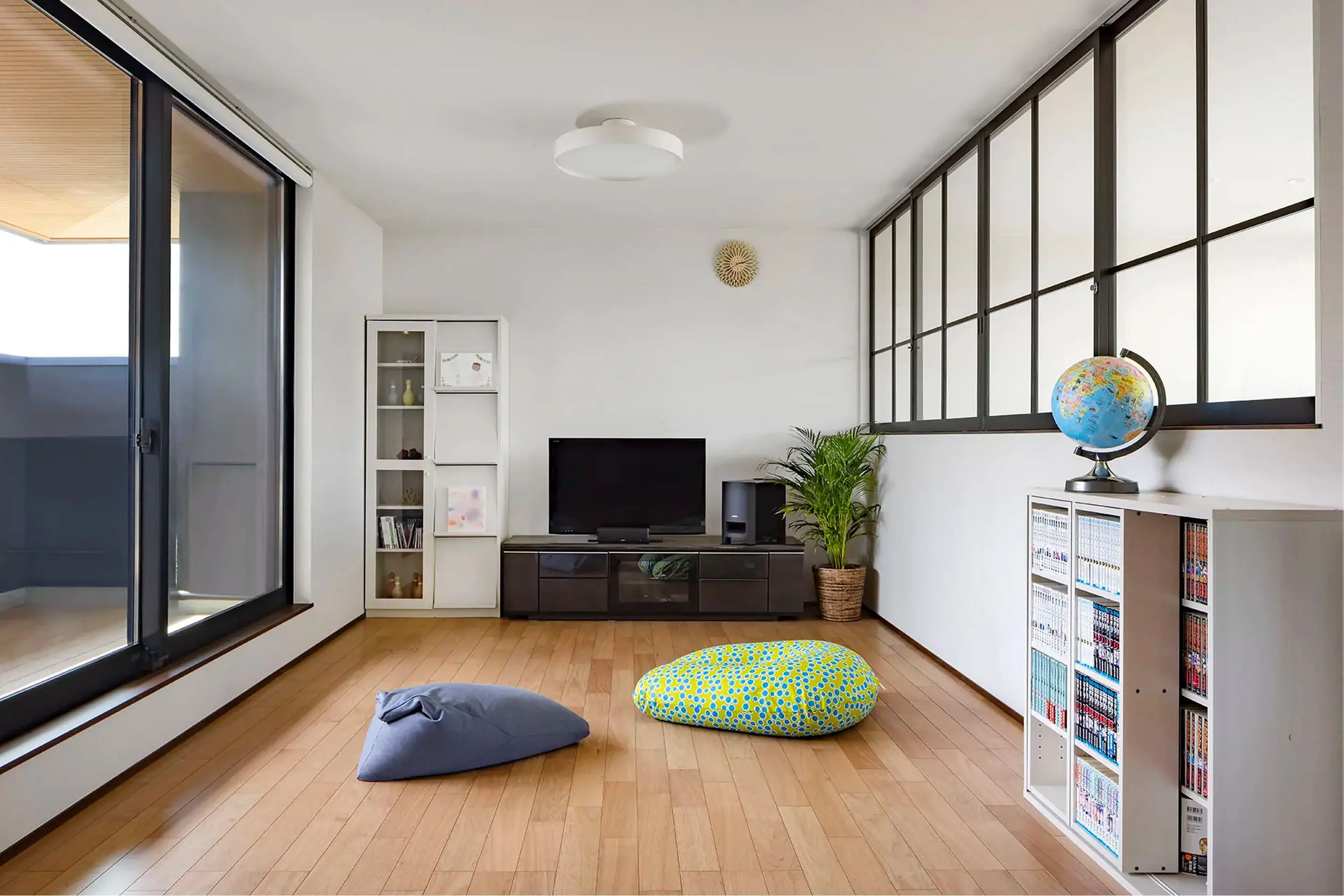 床にビーズクッションを置いたリビングで、テレビや本棚、観葉植物が配置された落ち着いた空間