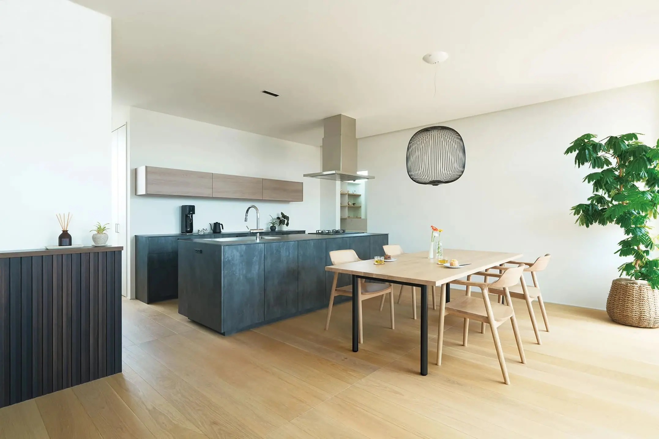 ナチュラルな木製ダイニングとダークグレーのキッチンが調和した、観葉植物が映える開放的なLDK空間