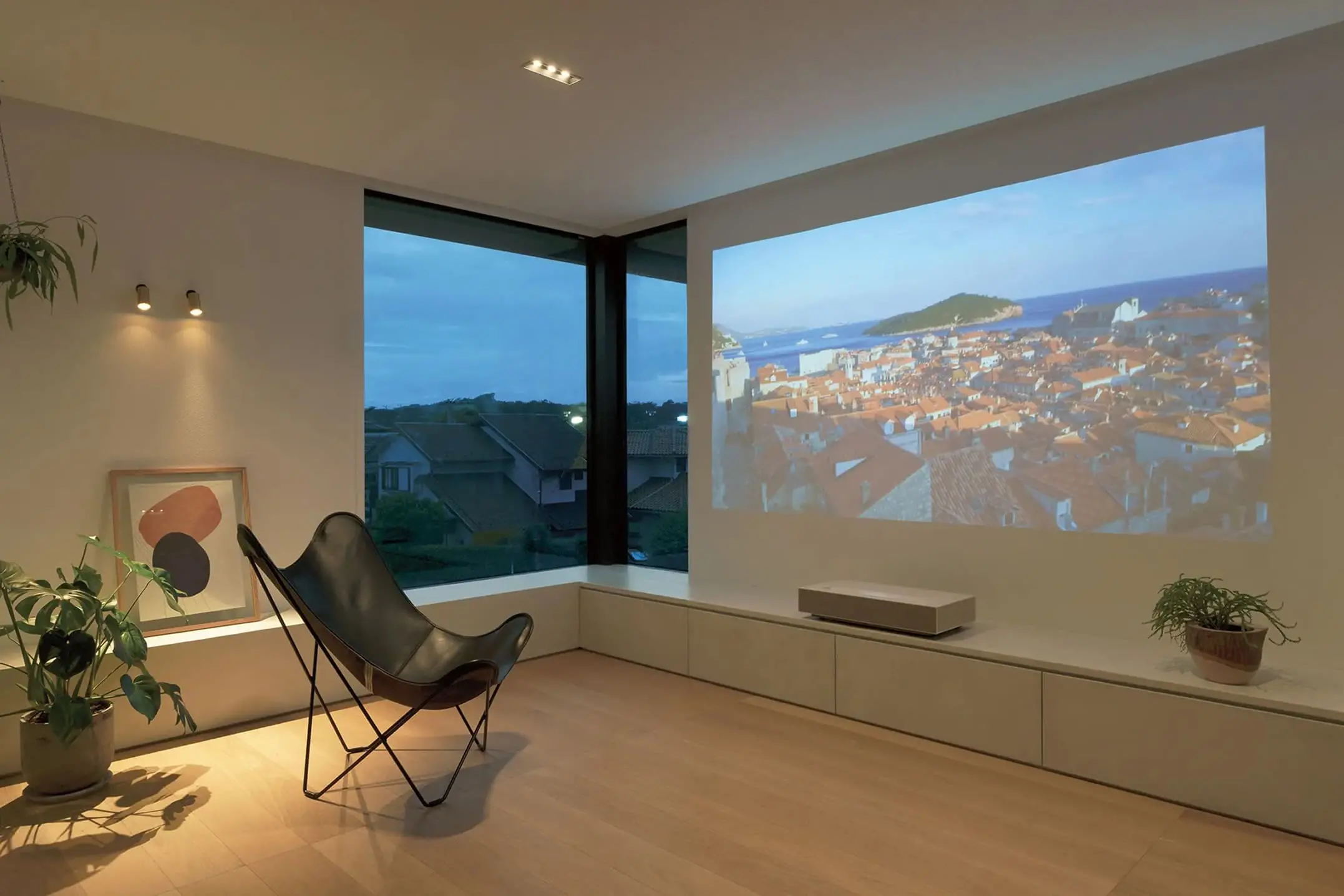 壁に大きく映像が投影されたホームシアター風のリビングで、落ち着いた照明と窓の夜景が印象的