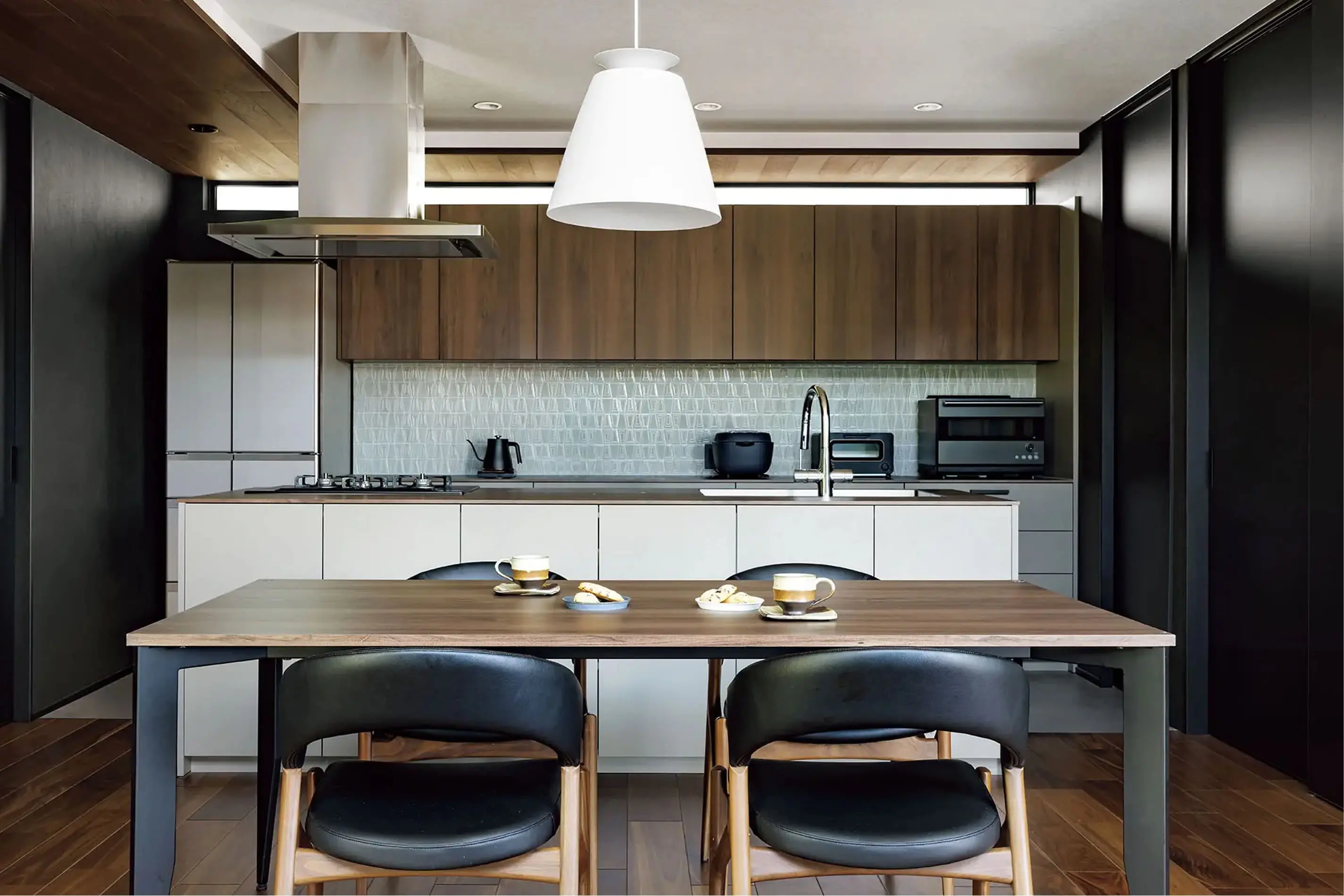 木目とブラックを基調としたシンプルモダンなキッチンで、ダイニングテーブルにはコーヒーとお菓子が並ぶ