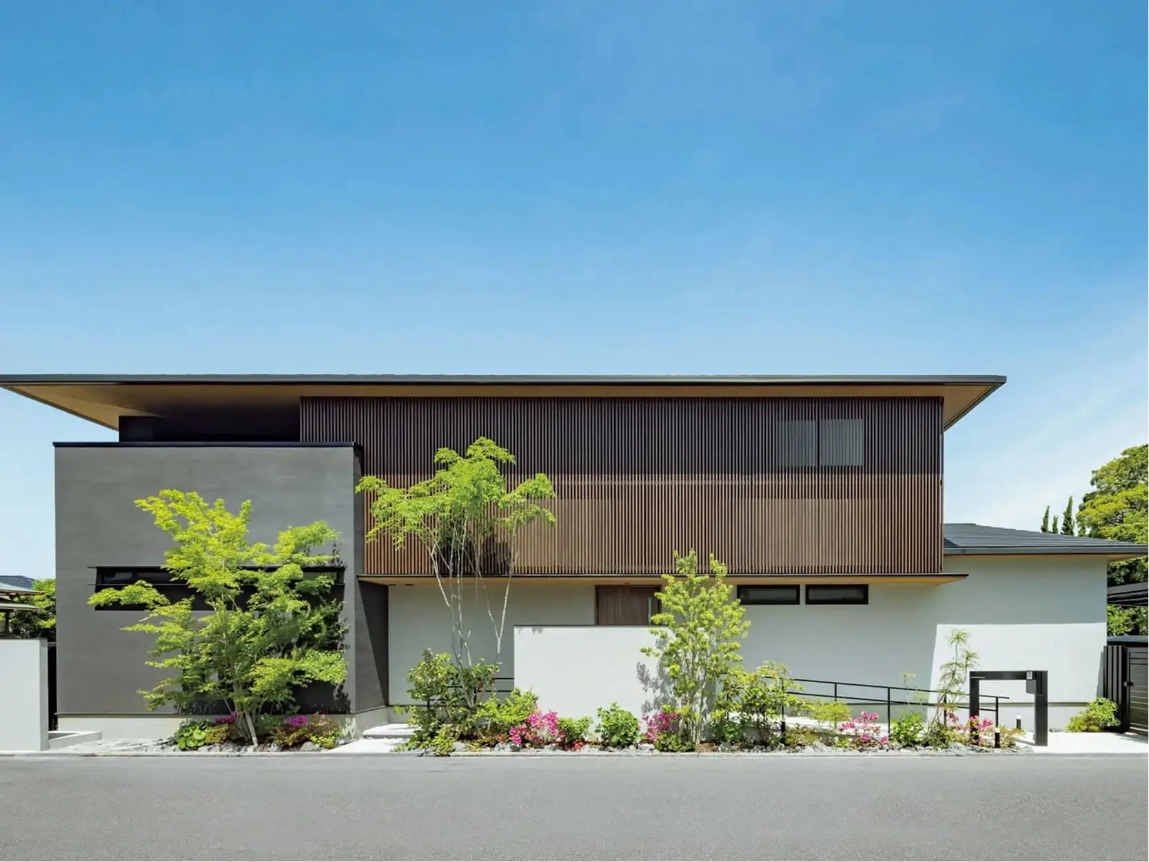 木と白を基調としたスタイリッシュな外観の二階建て住宅で、植栽が美しく整えられている