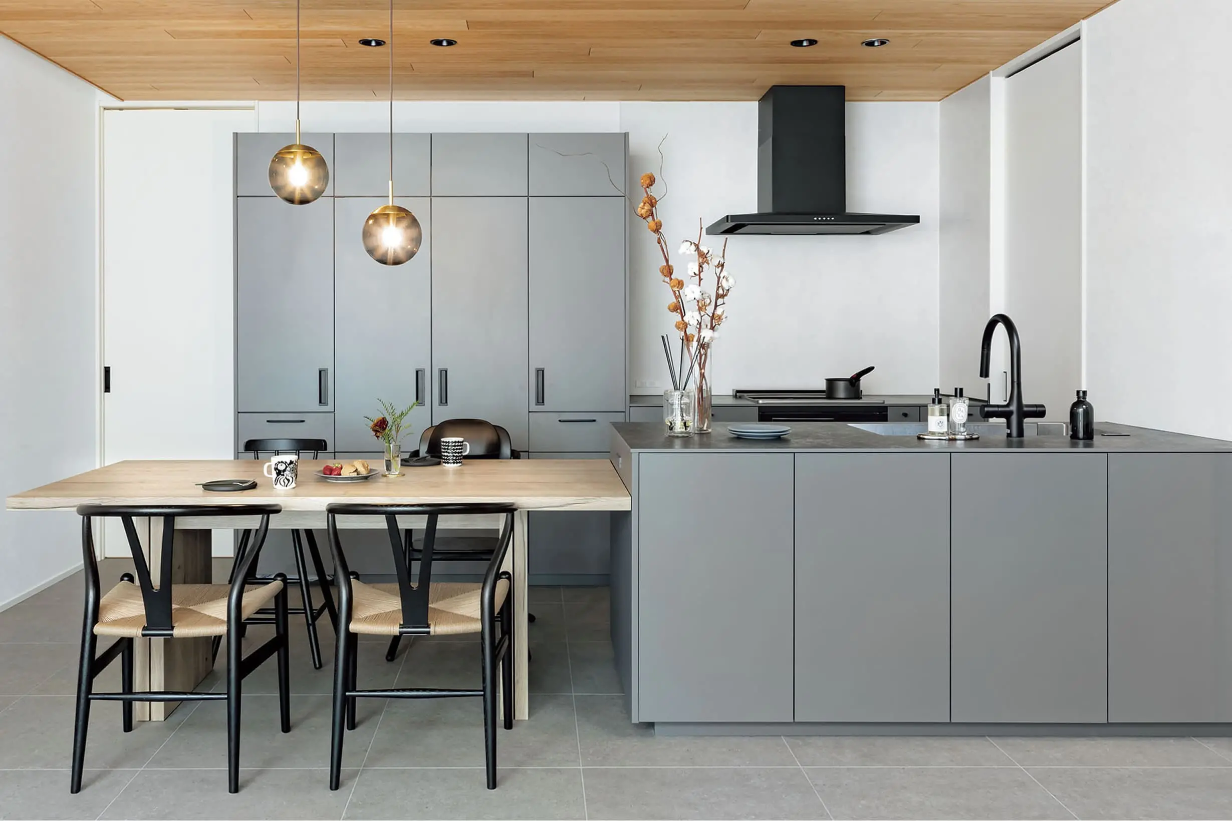 グレーを基調にしたモダンなキッチンで、木製ダイニングテーブルとペンダントライトが調和する空間