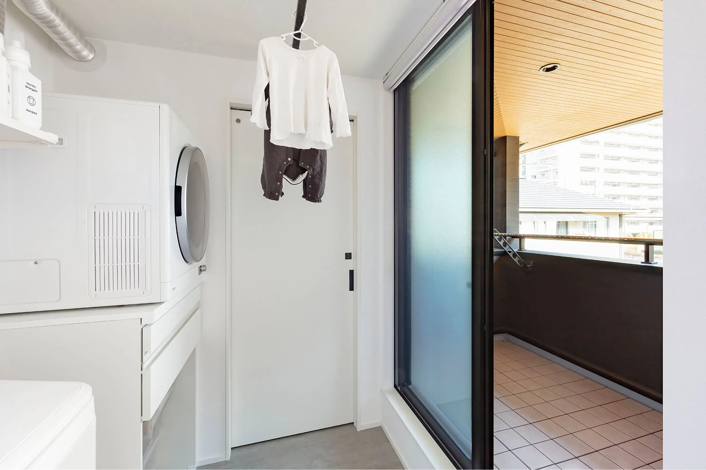 洗濯機のあるランドリールームからバルコニーへとつながる動線で、子ども服が室内干しされている様子