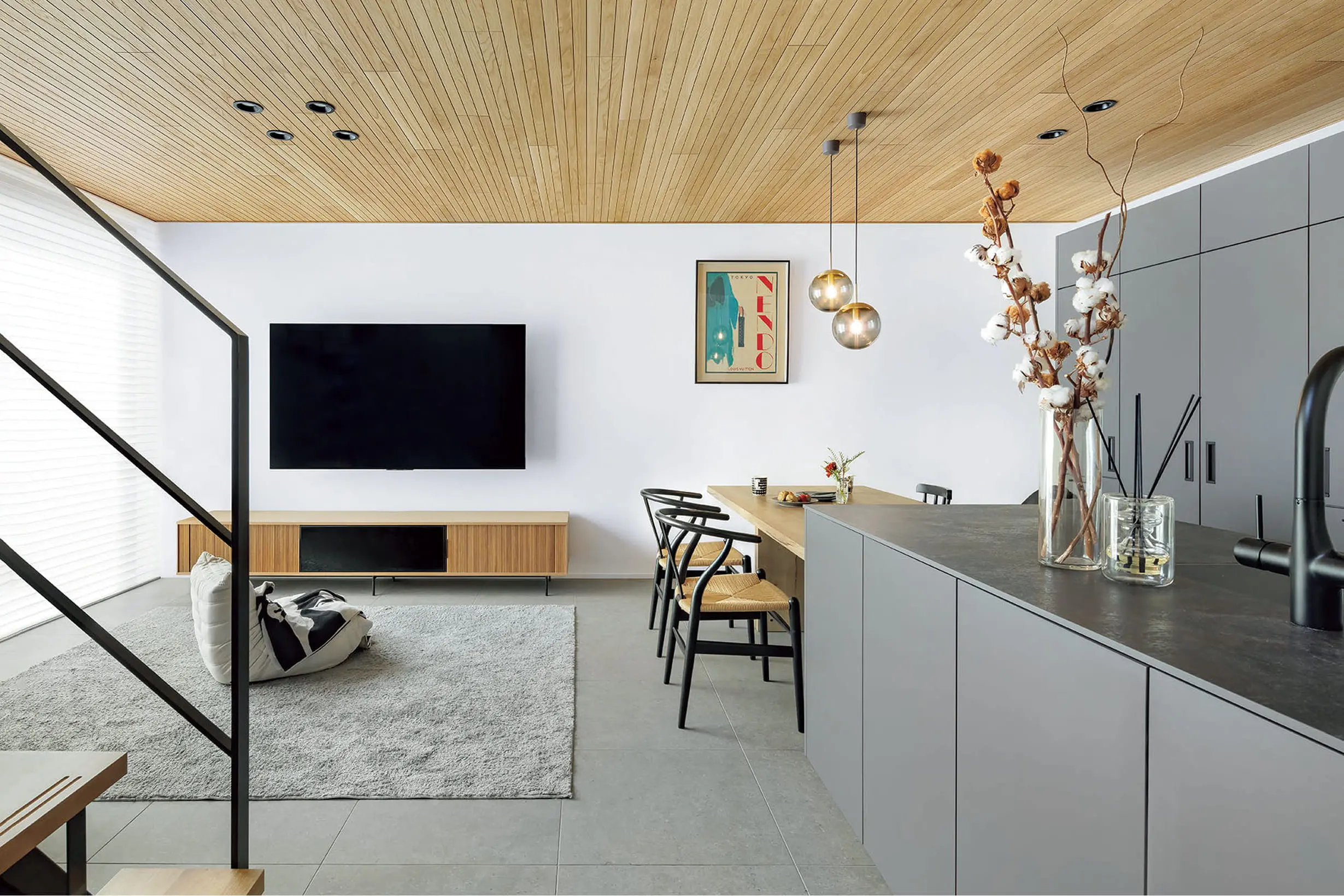 キッチンから続くリビングには大型テレビとラグがあり、ナチュラルな木目天井が温かみを演出
