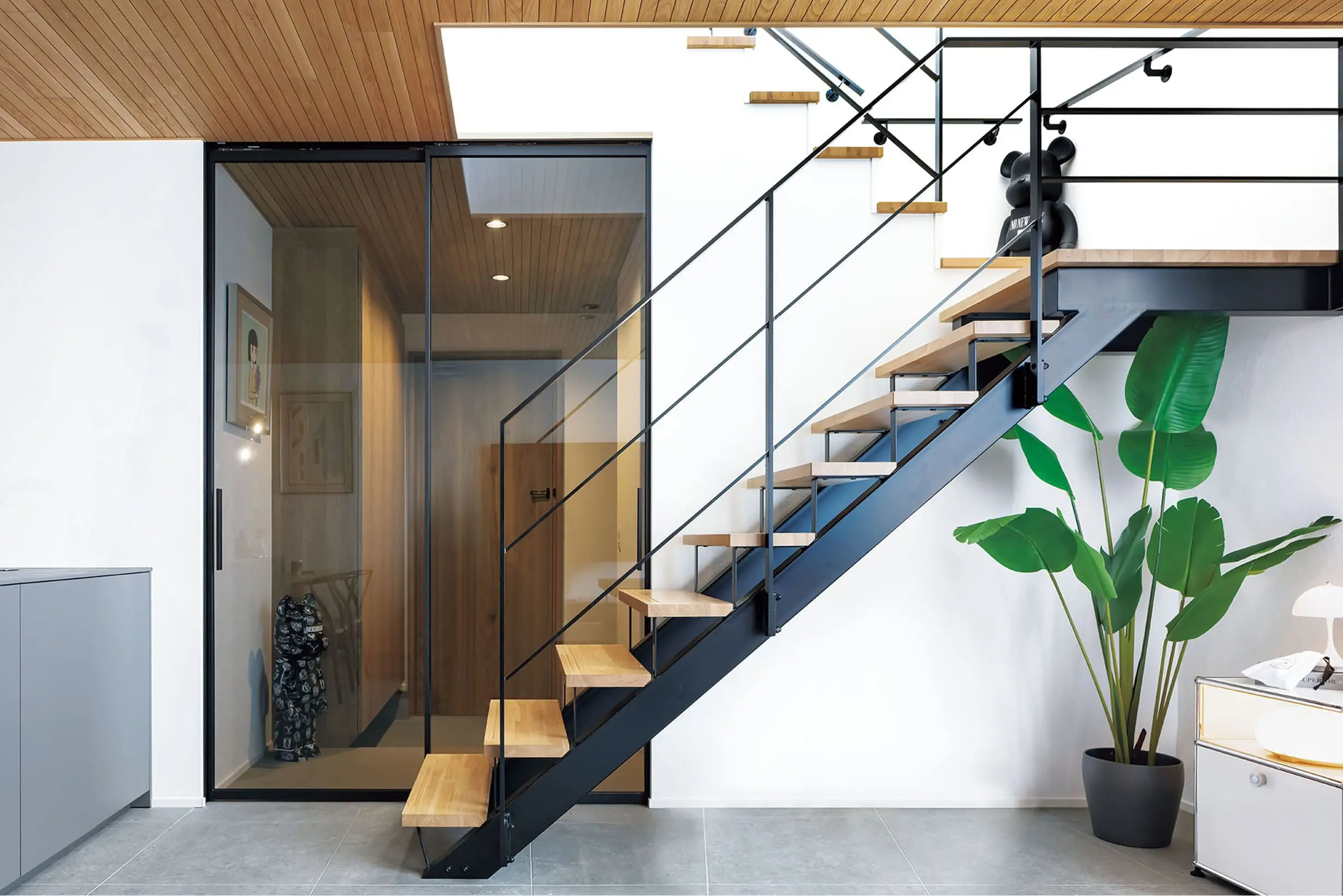 アイアン階段と大きな観葉植物が印象的な玄関ホールで、ガラスの間仕切りが空間を広く見せている